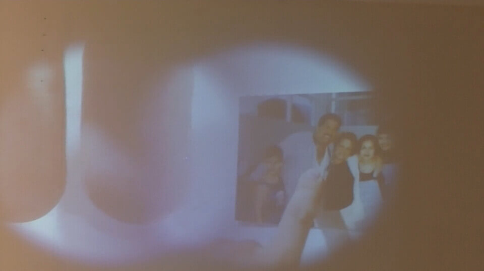 Wall projection in the shape of two overlapping circles. The left shows two fingers, close to the camera. The right shows a photo of a small boy, a large man, and three women of various ages.