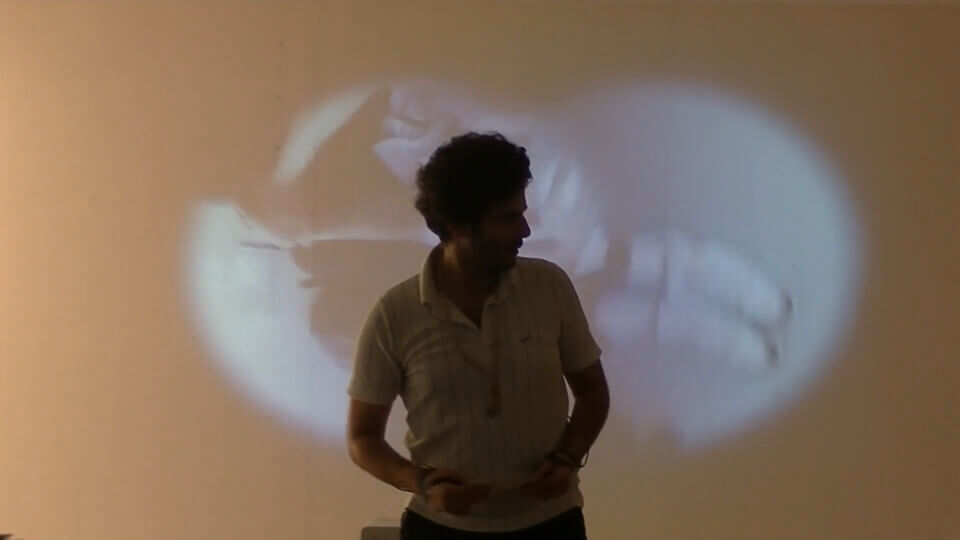 The performer stands in front of the dual-circle projection and looks to the side with this hands in front of his waist. The projection shows a sideways view of someone sitting in a chair.