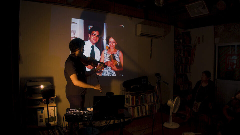 the performer plays viola in front of a projection of man and woman in their late 20s.