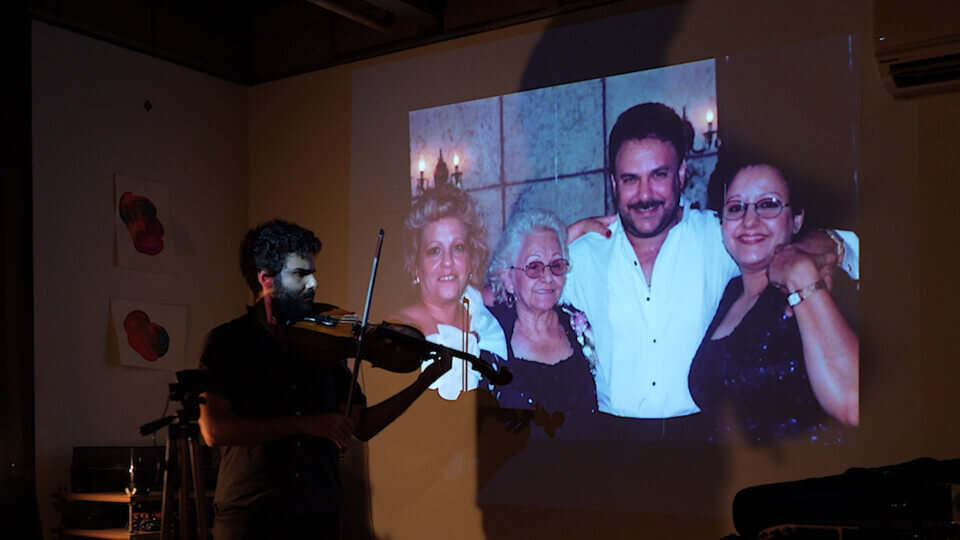 the performer plays viola in front of a projection of two women and a man in their 40s or 50s and older woman in her 70s