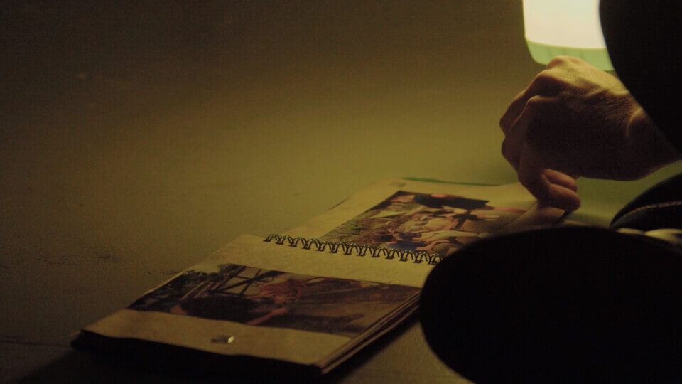 a hand turns through a photo album, lit by a lantern