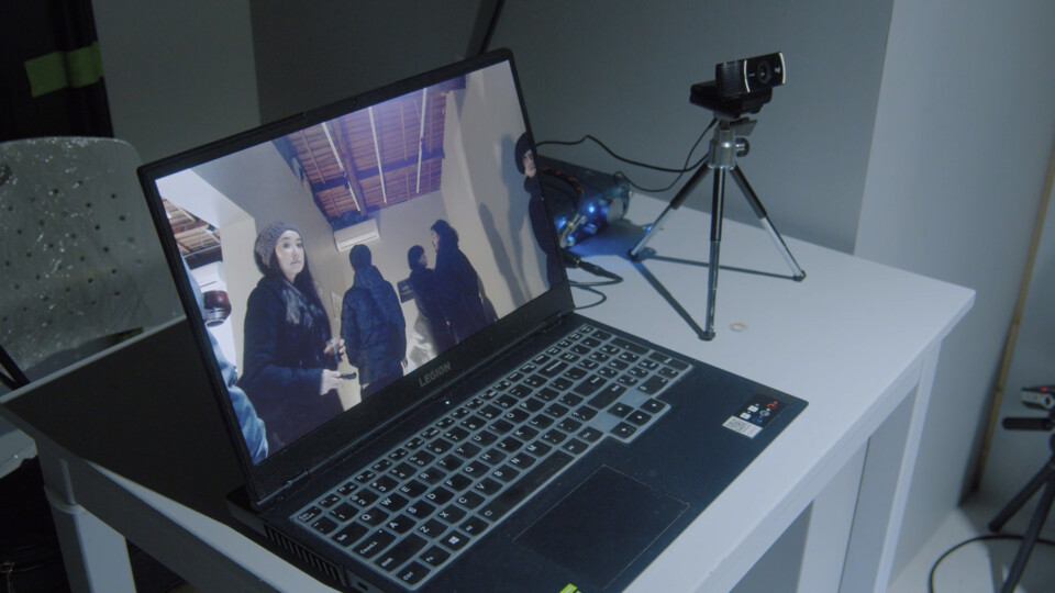 a laptop computer on a small table displays live footage of the event guests who look towards it. Next to the laptop is a webcam on a small tripod