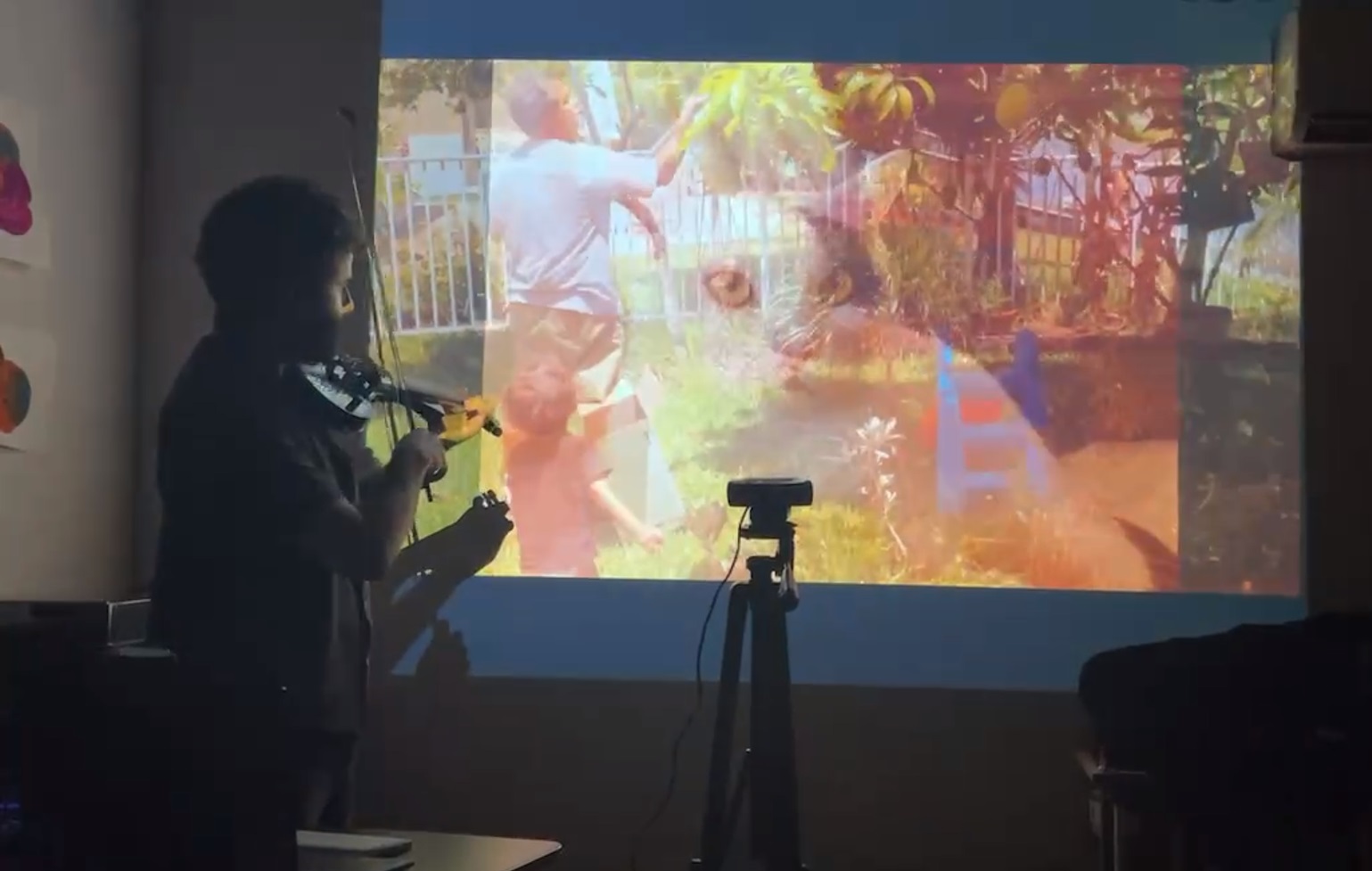stephan e perez playing a MIDI violin in front of a projection of composited images. The two images are of a man in a garden and a closeup of a cat.