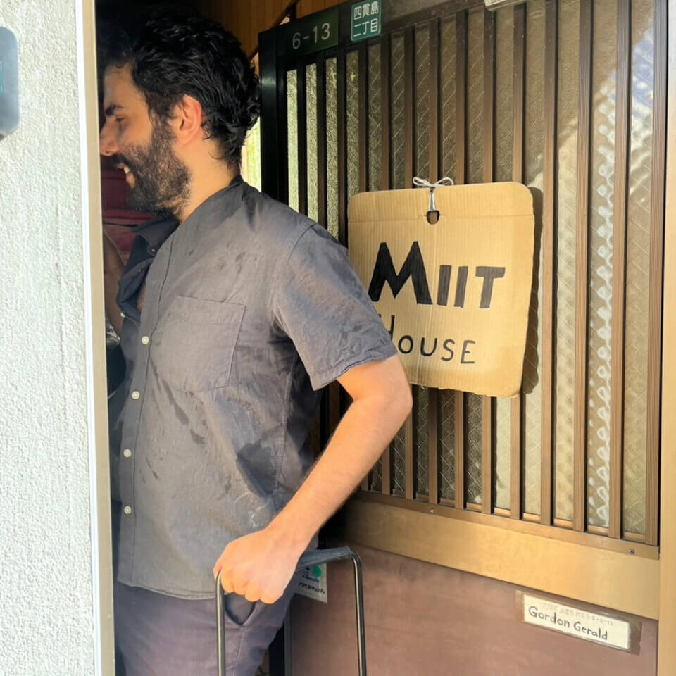 the performer, stephan e perez, walks into the front door of the venue, which has a sign reading 'Miit House' on it