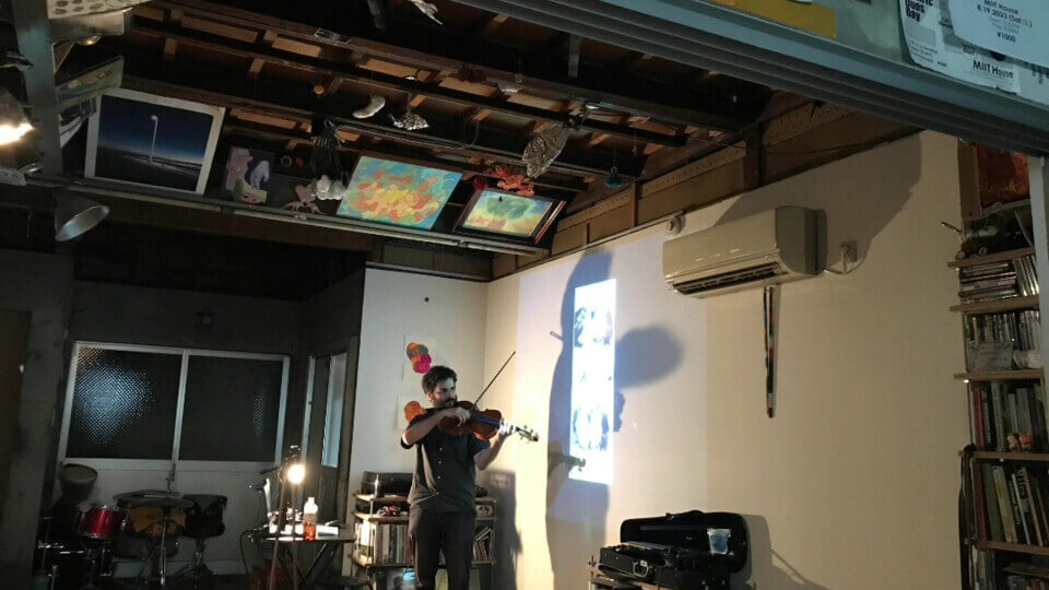 the performer playing the viola in front of a wal projection. The projection shows two photo-booth photos of a man and woman in their early 20s. The event hasn't started yet so the room is well lit.