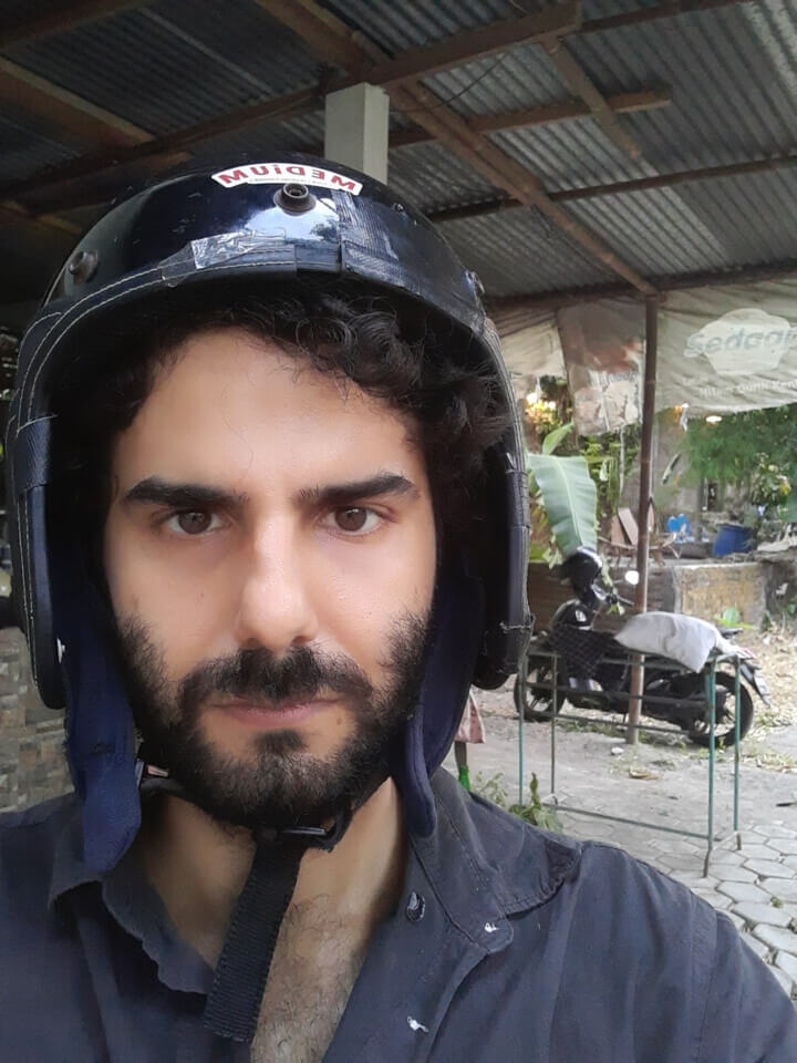 pre-event photo. stephan wears a black helmet, strapped around his chin. In the distance, you can see a parked moped.